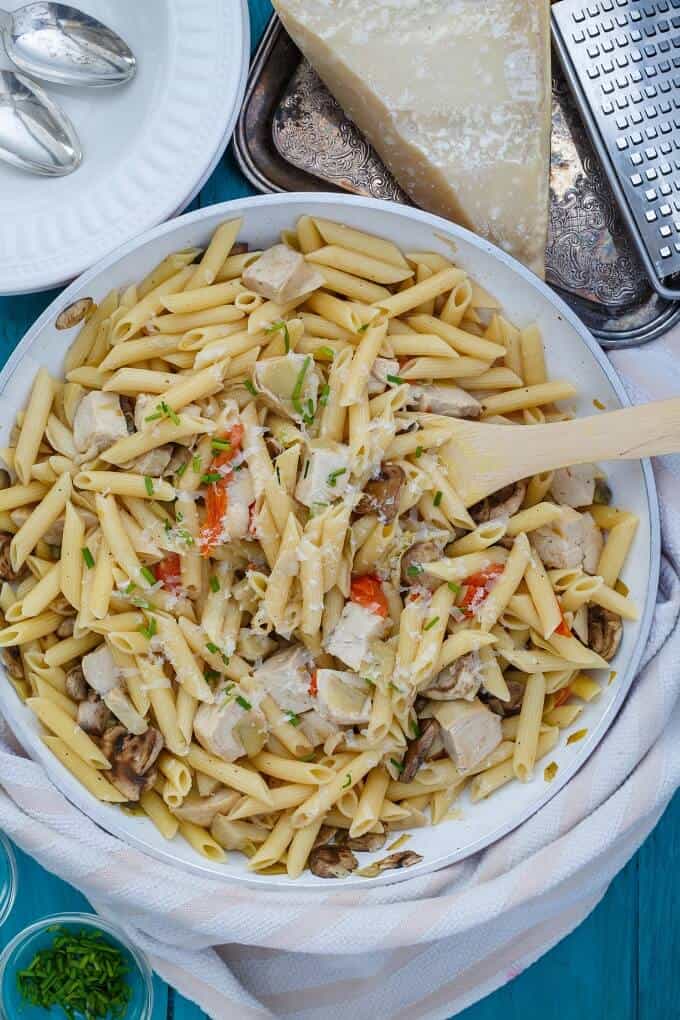 One Pan Creamy Chicken Pasta in white bowl with wooden spatula next to cheese on tray with grater and white plate with spoons (Barilla Pronto)