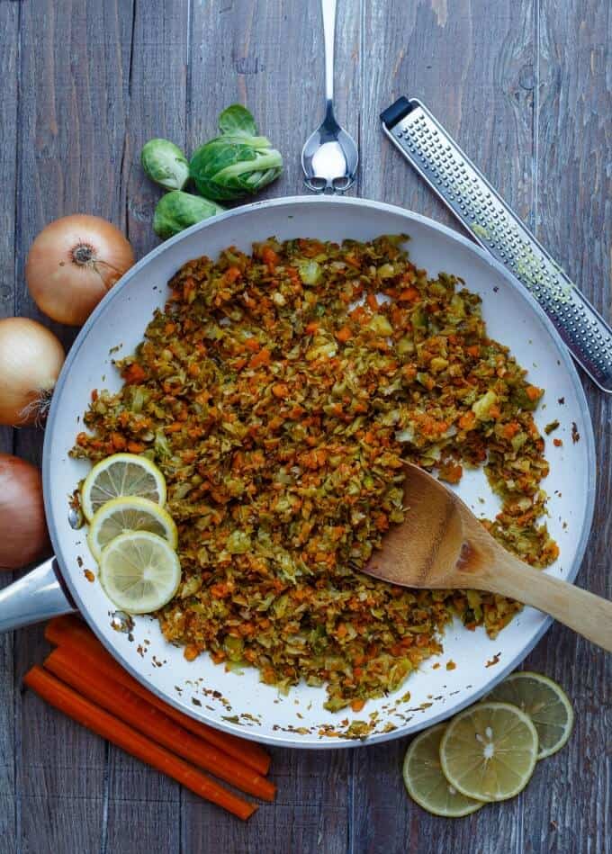 Shredded Lemon Brussels Sprouts Saute  on pan with wooden spatula on table with lemons ciles, carrots, onion, cale, spoon,cale, grater