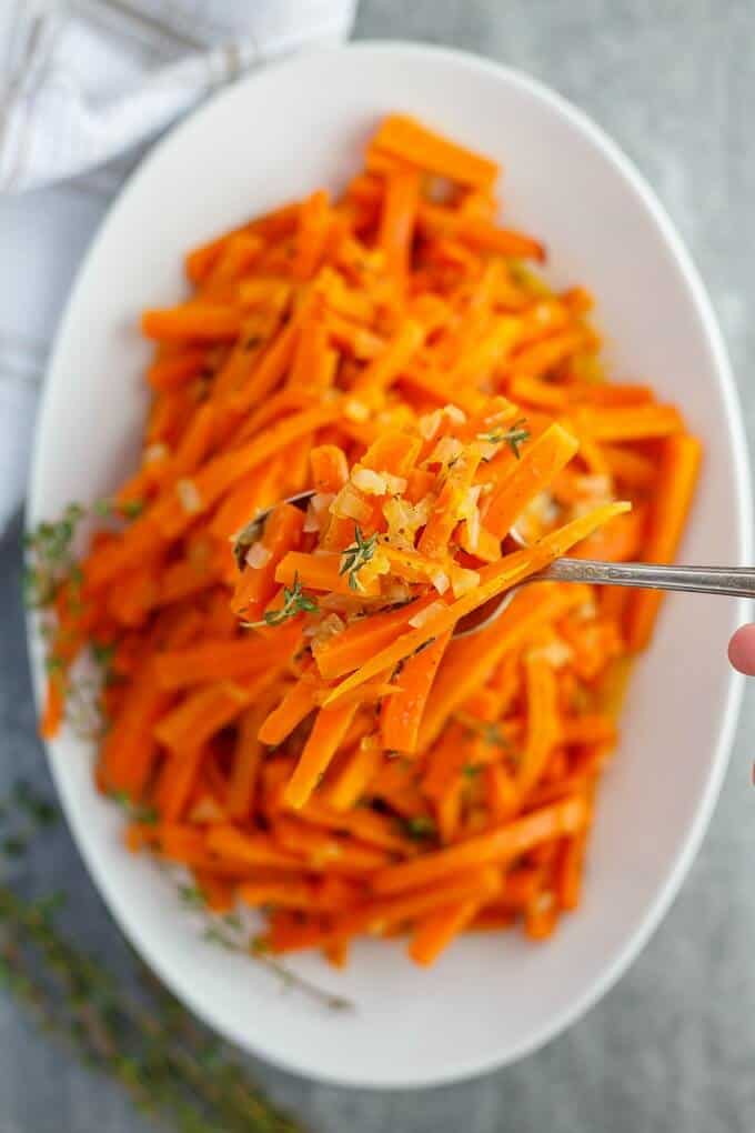 Slow Cooker Lemon Thyme Butter Carrots on white tray, picked by spoon