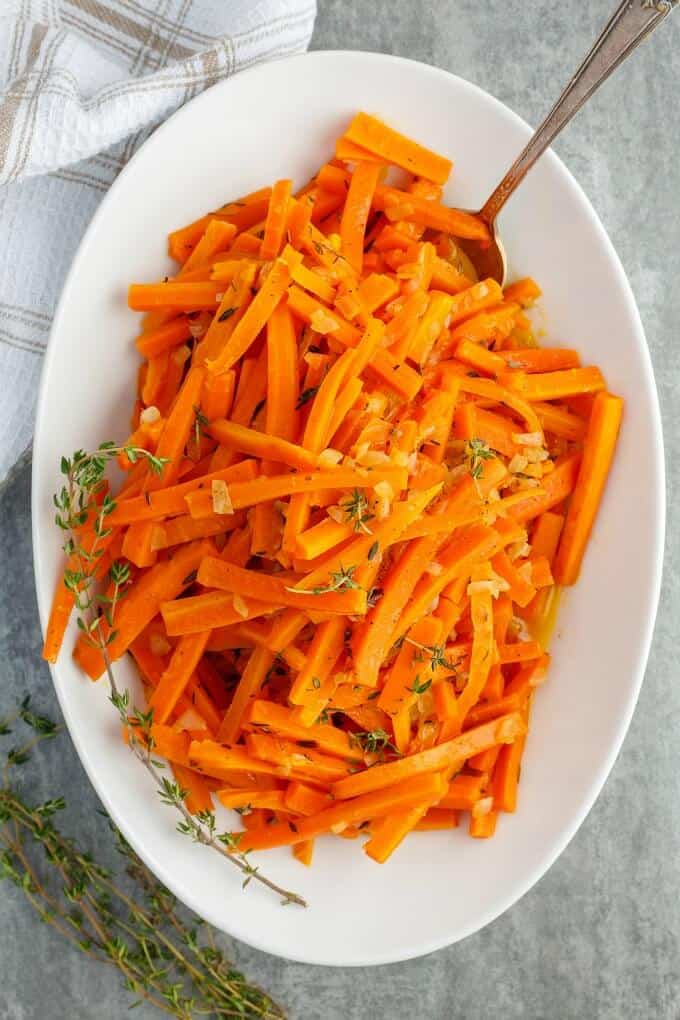 Slow Cooker Lemon Thyme Butter Carrots on white tray with spoon next to cloth wipe