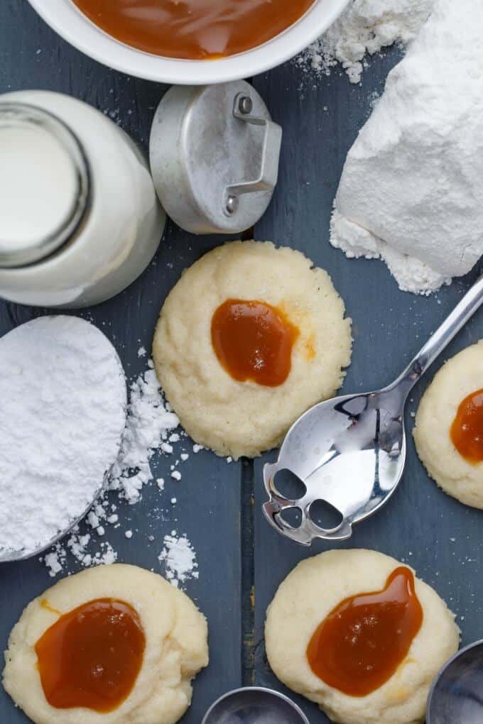 Thumbprint Caramel Shortbread Cookies on gray table with spoon, jar of milk with lid and flour