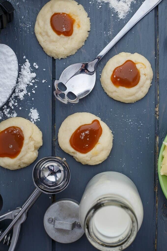 Thumbprint Caramel Shortbread Cookies on gray table with spoons, jar of milk