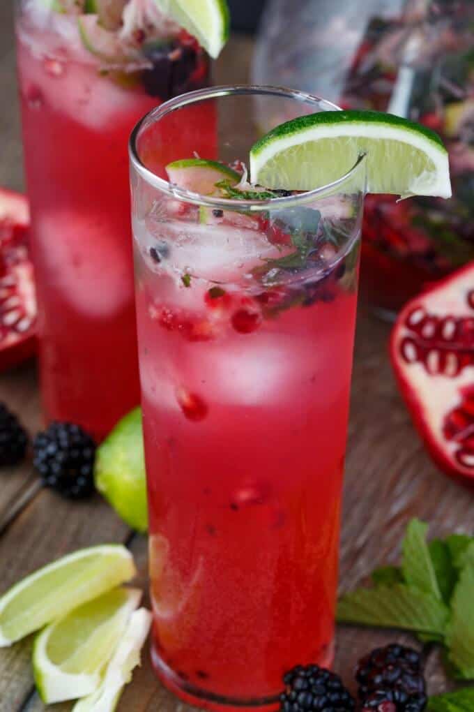 Pomegranate Blackberry Mojitos in glass cups with lime slices, blackberries, pomegranate on the table