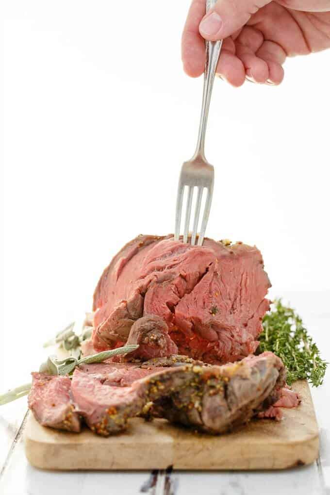 Slow Cooker Herb Butter Inside Round Roast on wooden pad with herbs, fork held by hand