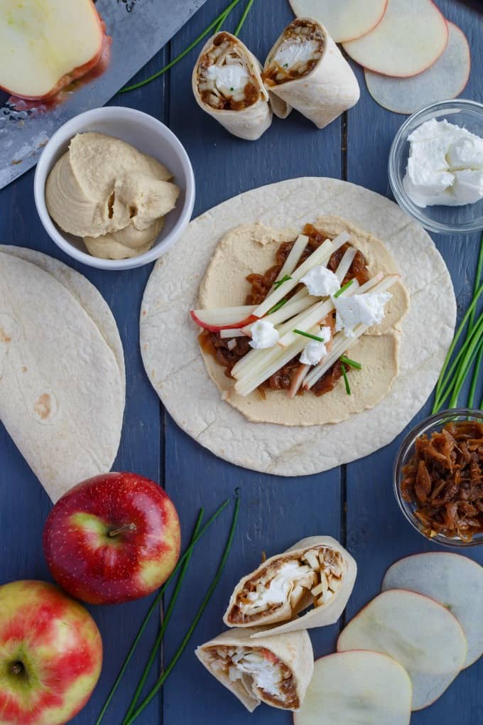 Caramelized Onion Apple Wraps with Hummus on blue table with herbs and apples