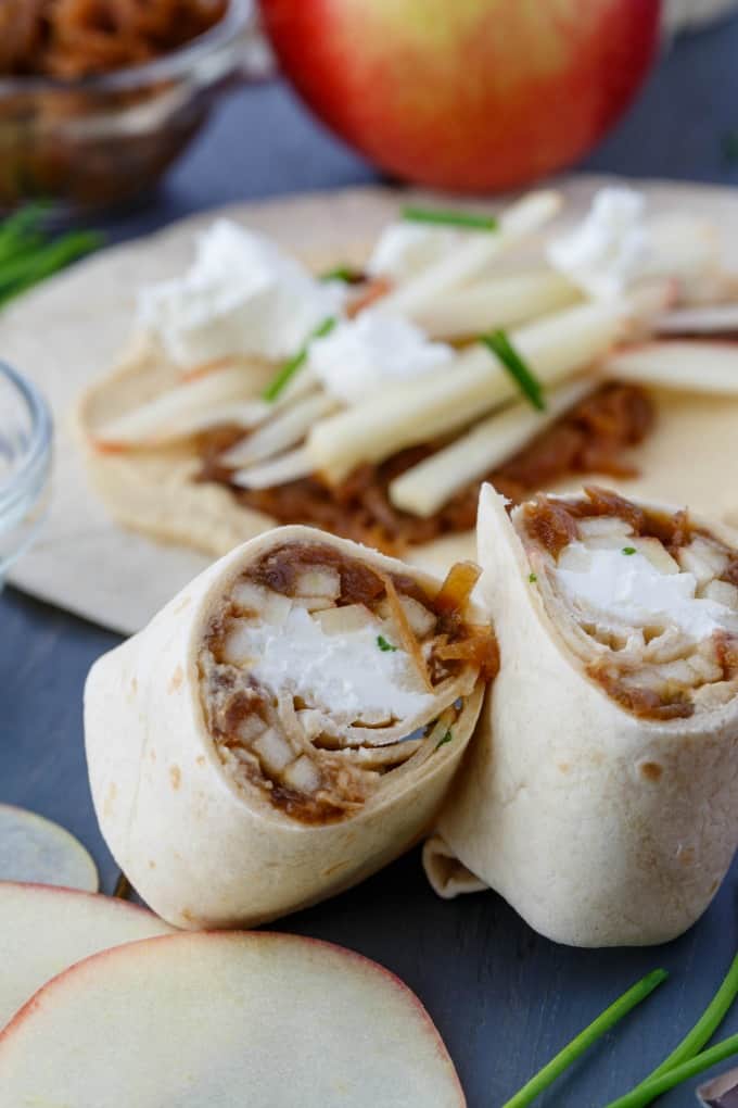 Caramelized Onion Apple Wraps with Hummus on blue table with herb and apple