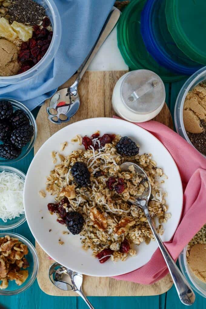 Homemade Instant Oatmeal on white palte with fruits, nut and spoon , wooden pad with jark of milk, bowls of ingredients on table