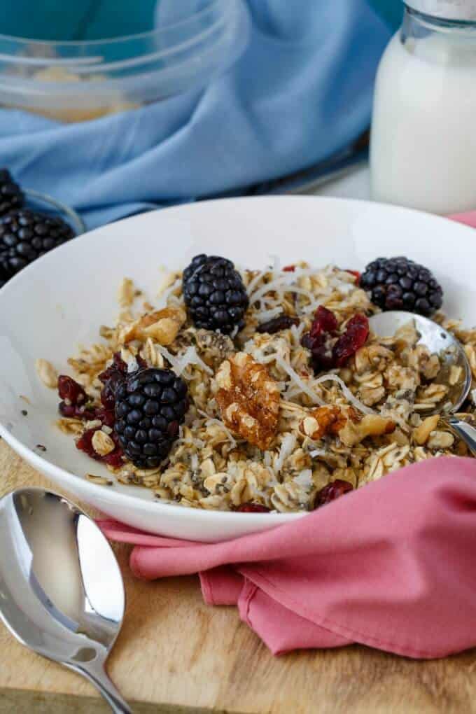 Homemade Instant Oatmeal on white plate with spoon and fruits and nuts, pink wipe cloth on wooden pad