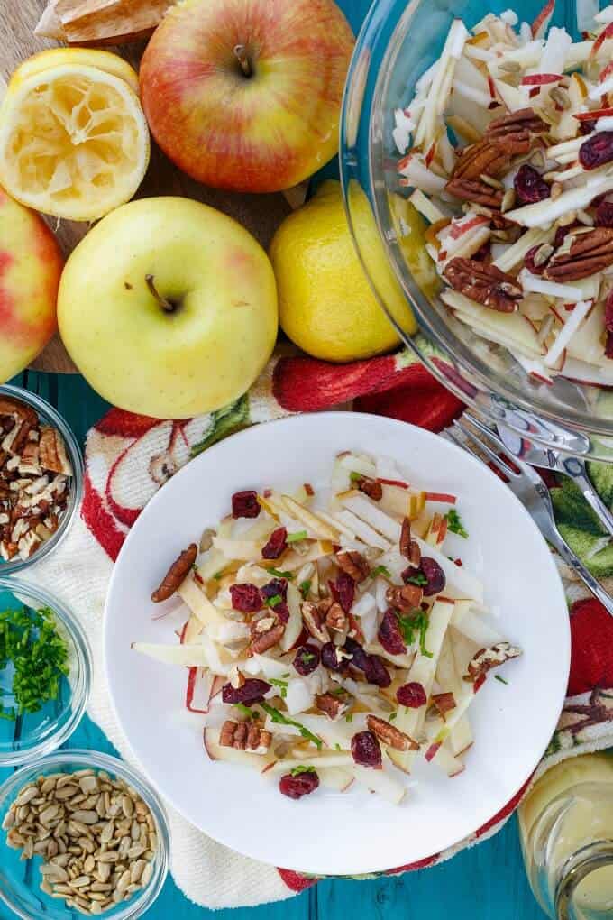 Raw Apple Salad (Vegan & GF) on white plate and in glass bowl on table with apples, ingredients, forks in bowls and cloth wipe 