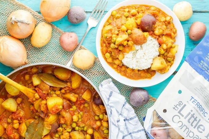 Vegan Potato Curry over Cauliflower Rice on white plate and in pan on blue table with fork, sack of spilled potatoes