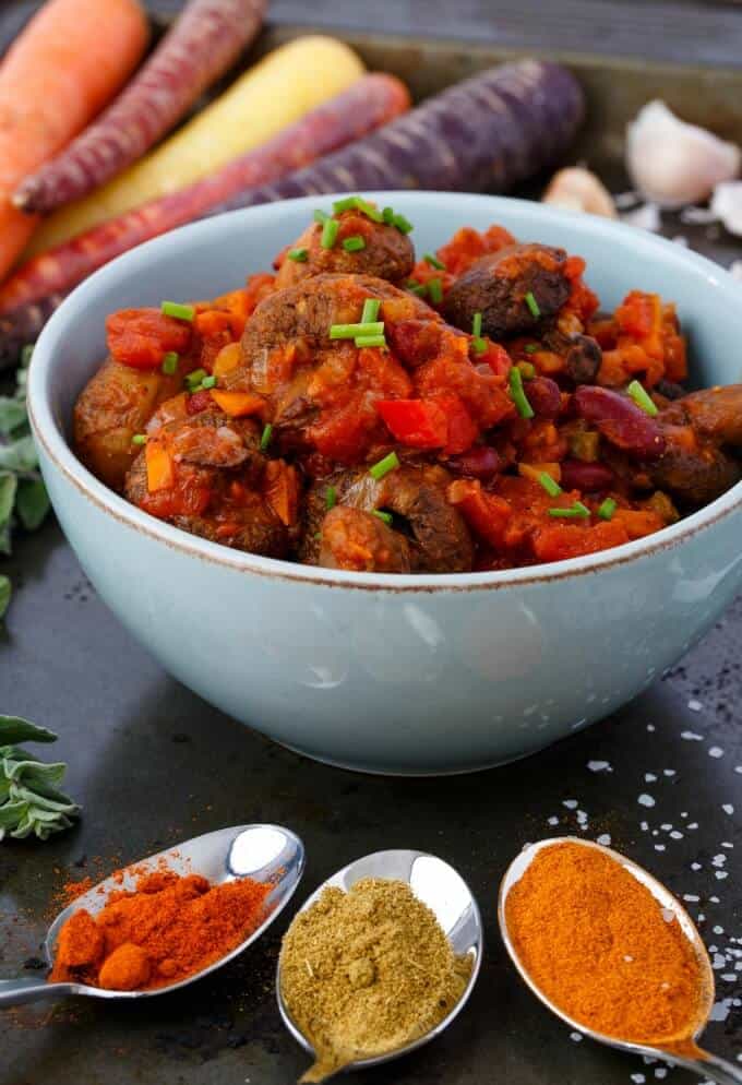 Whole Roasted Mushroom Chili in blue bowl with vegetable and ingredietns on spoon on black table