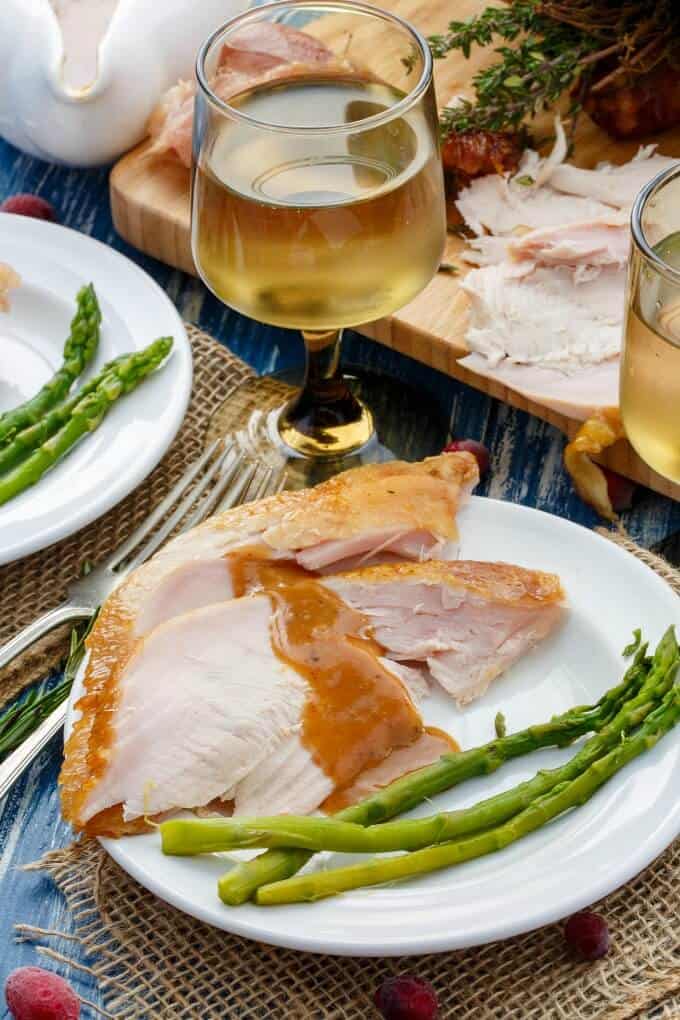 Smoked Turkey on white plates and wooden pad with vegetables on blue table with wine glasses