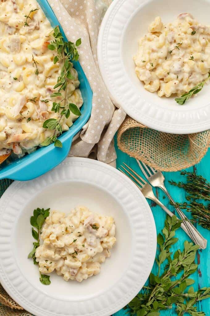 Leftover Smoked Turkey Mac and Cheese with Bacon on white plates and in blue casserole with herbs, more herbs and forks on blue table