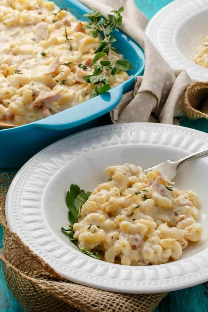 Leftover Smoked Turkey Mac and Cheese with Bacon on white plate with fork and herb, in blue casserole with herb