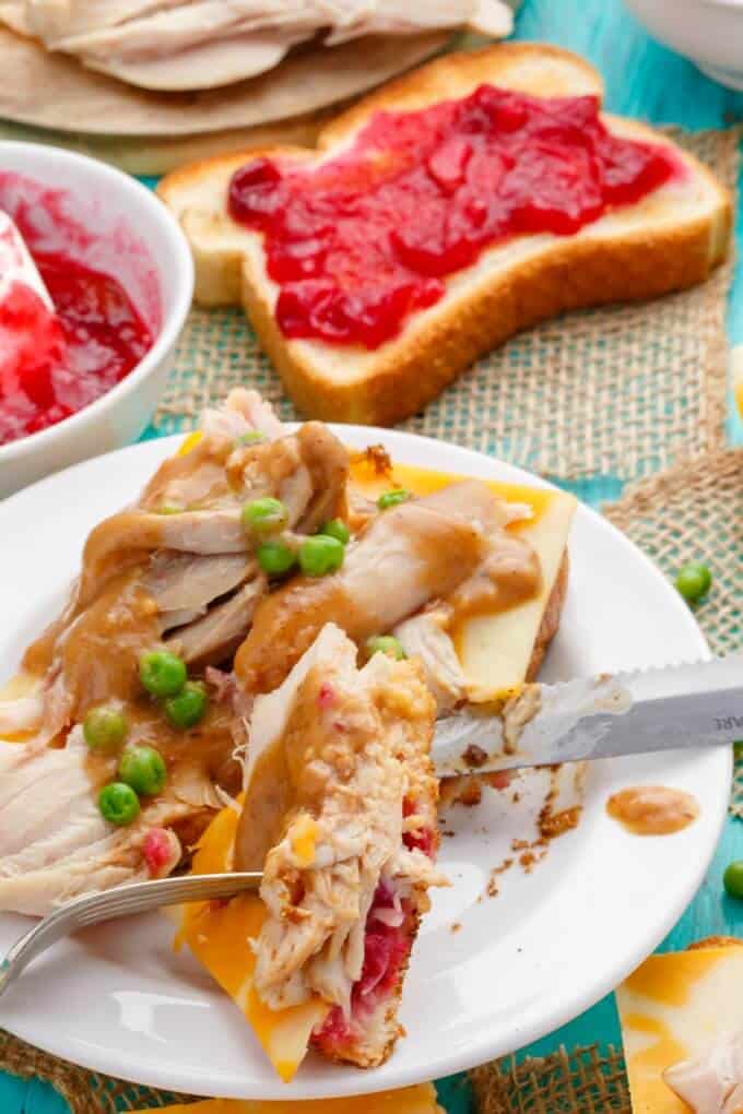 Open-Faced Turkey Sandwiches (Using Leftover Turkey) on white plate with knife and fork with sandwich with jam in the background