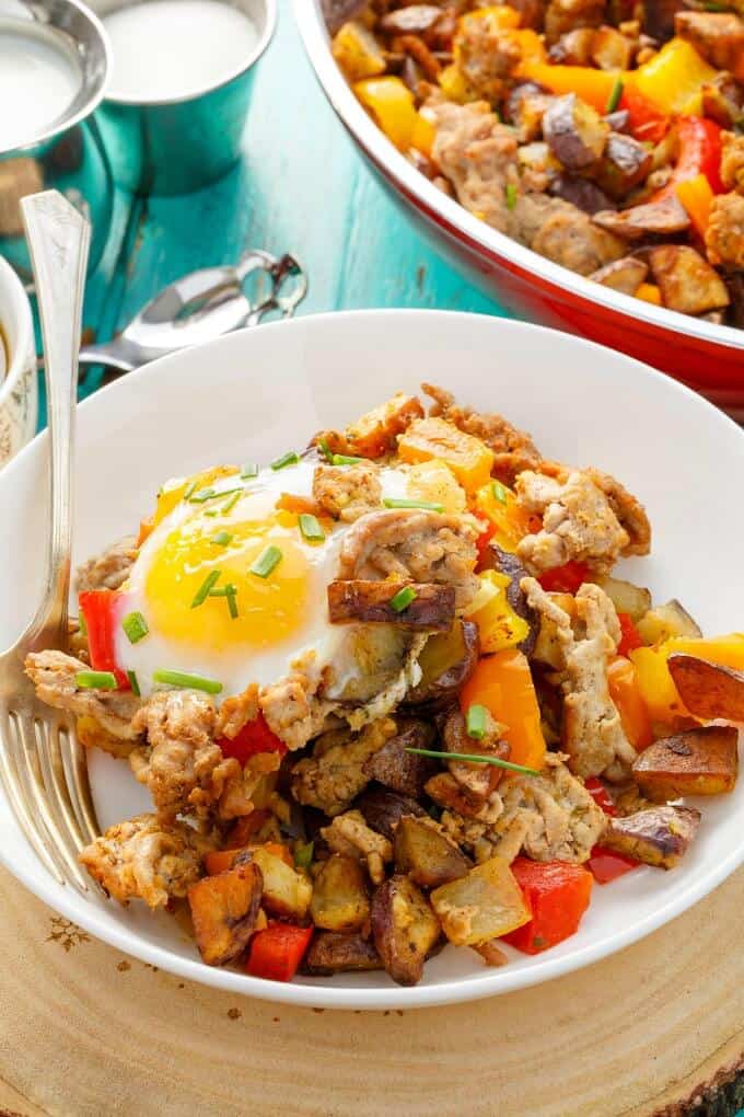 Turkey Potato Hash on white plate with fork and in pan on blue table with spoon, ingredients