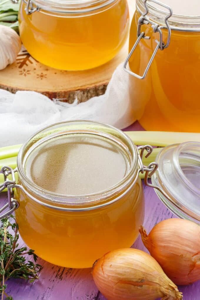 Homemade Turkey Stock in glass jars with onions and other vegetables around