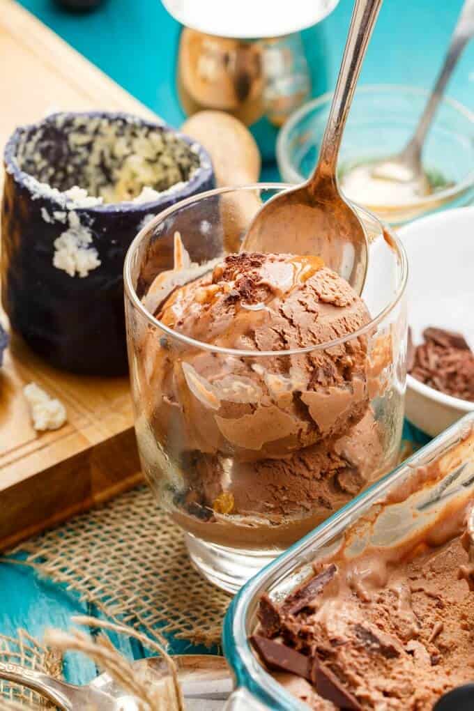 Dark Chocolate Blue Cheese Ice Cream with Honey in glass cup with spoon, glass container, jar of cheese, wooden pad, bowls with ingredients on blue table