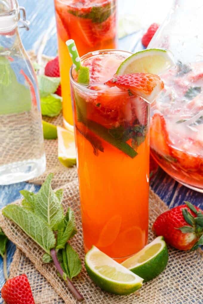 Fresh Strawberry Mojitos in glass cups with freshly sliced fruits with straws, ripe strawberries and limes on the table