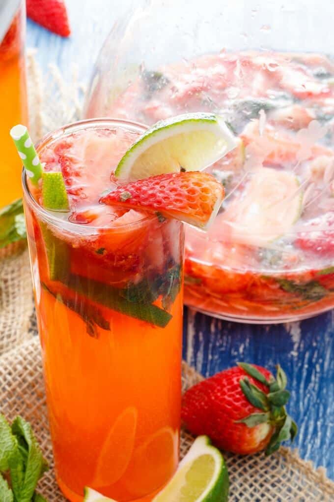 Fresh Strawberry Mojitos in glass cup with straw and in glass pitcher with fresh sliced fruits, ripe strawberry and lime on the table