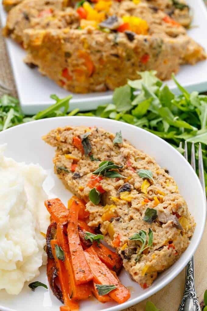 Slow Cooker Turkey Meatloaf on white plate with carrots and mashed potatoes, rest of meatloaf on white tray on table with herbs and fork (Veggie Loaded!)