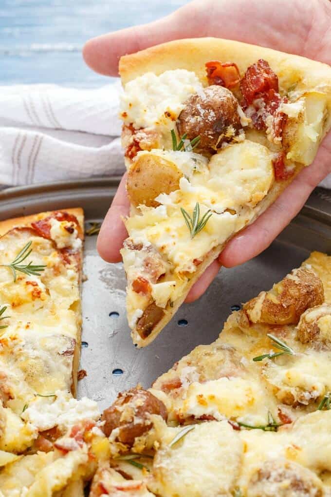 Thin Crust Bacon Potato Pizza on gray tray, one slice held on hand