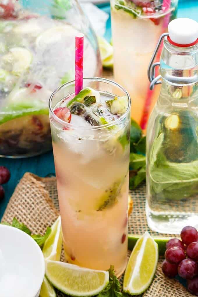 Fresh Kiwi-Grape Mojitos in glass cups and pitcher with straws, fresh limes and grapes on the table with glass bottle