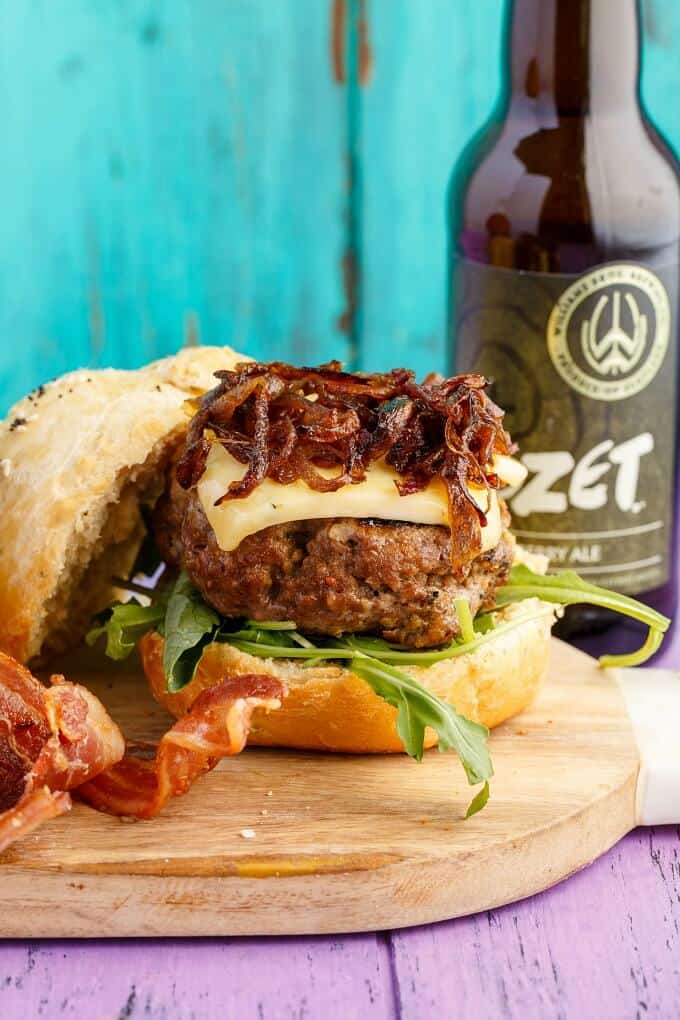 Homemade Honey-Garlic Hamburgers with Maple-Bacon Caramelized Onions on wooden pad, glass bottle in the background