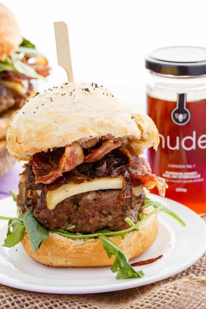 Homemade Honey-Garlic Hamburger with Maple-Bacon Caramelized Onions on white plate with honey jar in the background