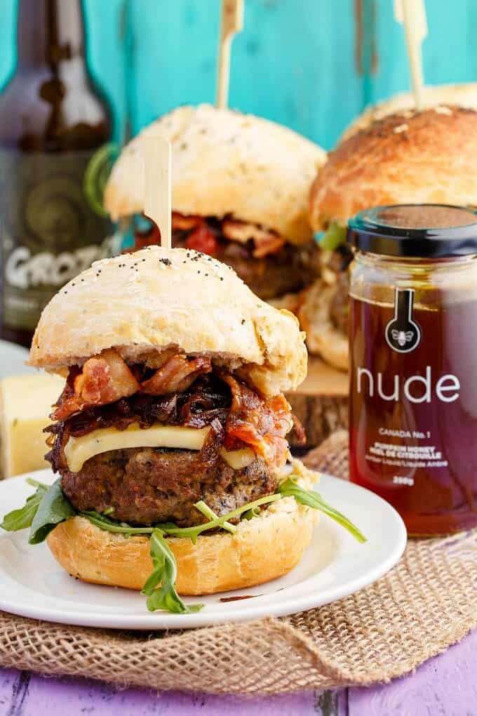 Homemade Honey-Garlic Hamburgers with Maple-Bacon Caramelized Onions on white plate and wooden pad with glass jar with honey,glass bottle in the background