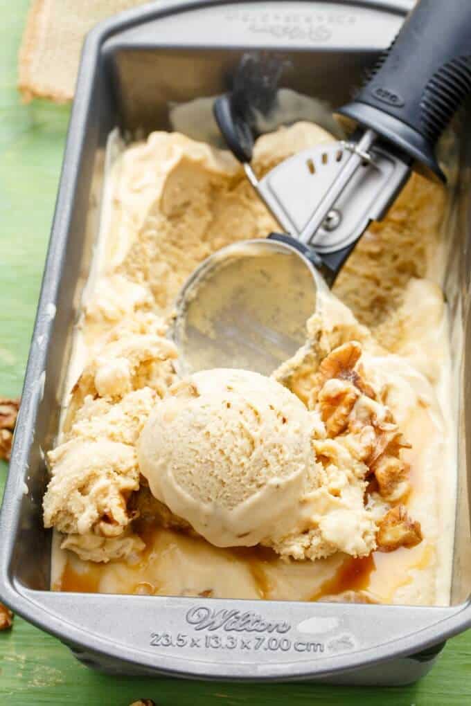 Homemade Maple Walnut Ice Cream in container with ice cream spoon on green table