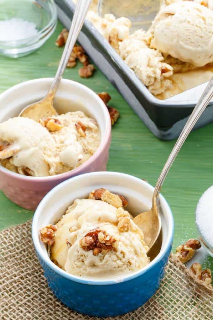 Homemade Maple Walnut Ice Cream in pink and blue bowls with spoons, container of ice cream in the background