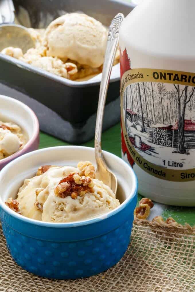 Homemade Maple Walnut Ice Cream in blue bowl with spoon, ice cream container and jug  of milk in the background