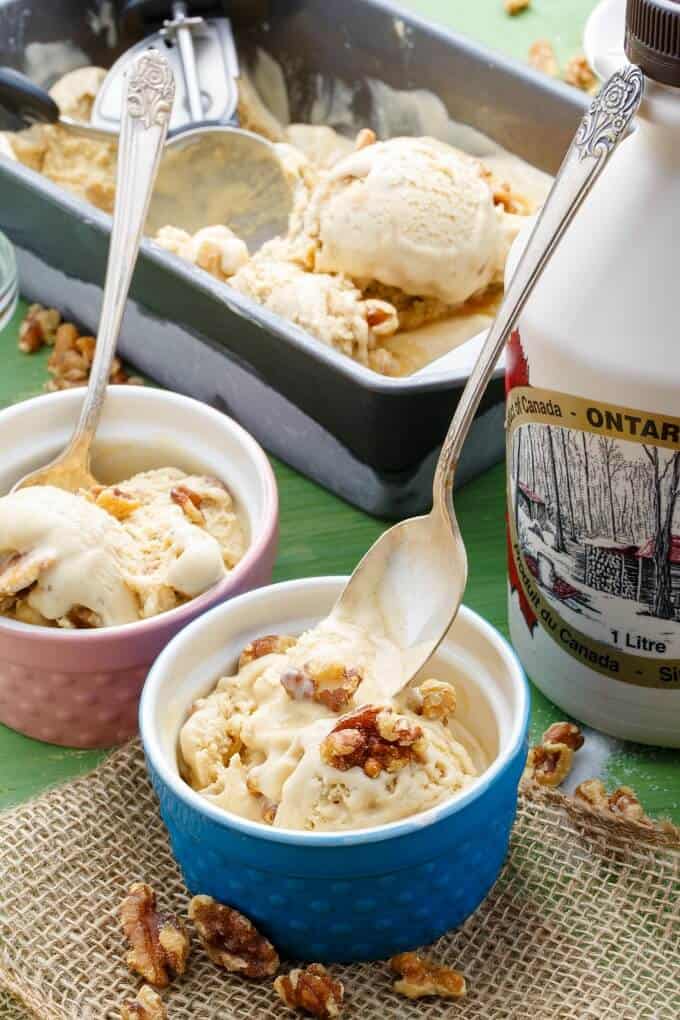 Homemade Maple Walnut Ice Cream in blue and pink bowl with spoons, jug of milk and container of ice cream in the backgorund