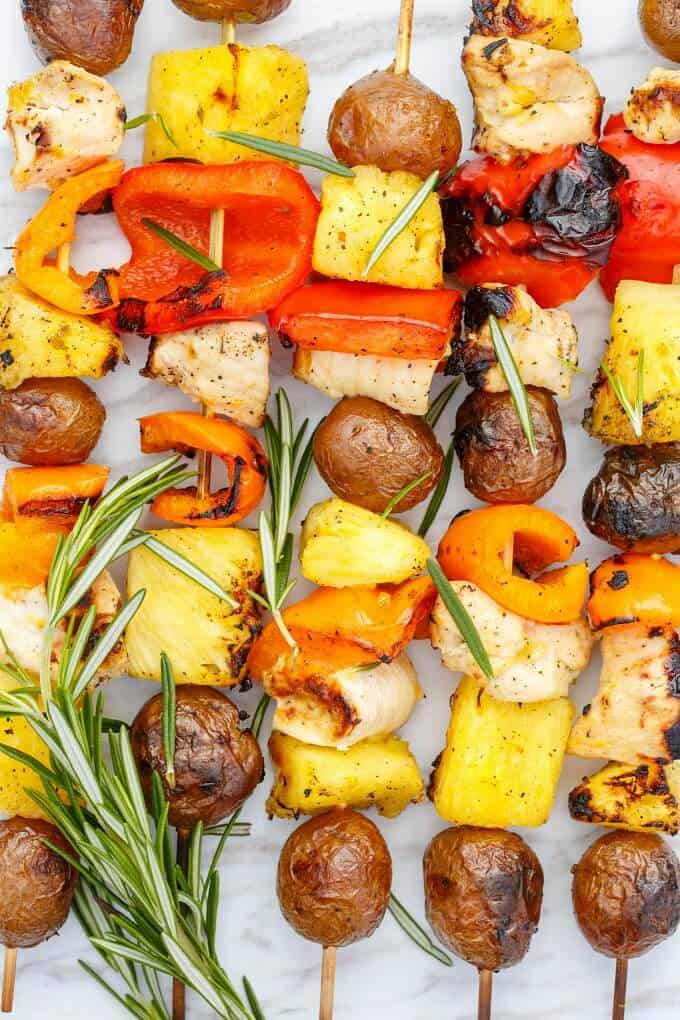 Orange Chicken Pineapple Potato Kabobs with herbs on white table