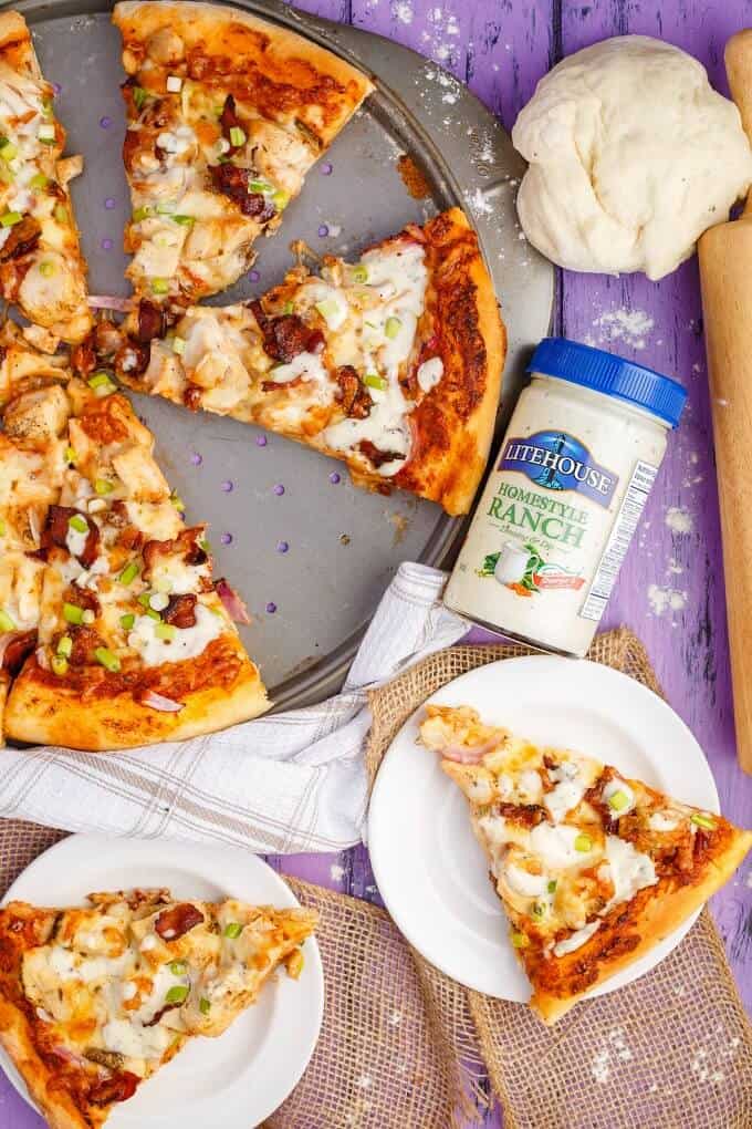 Chicken Bacon Ranch Pizza on gray tray and on white plates. Dressing in jar, pizza dough and wooden roller on purple table