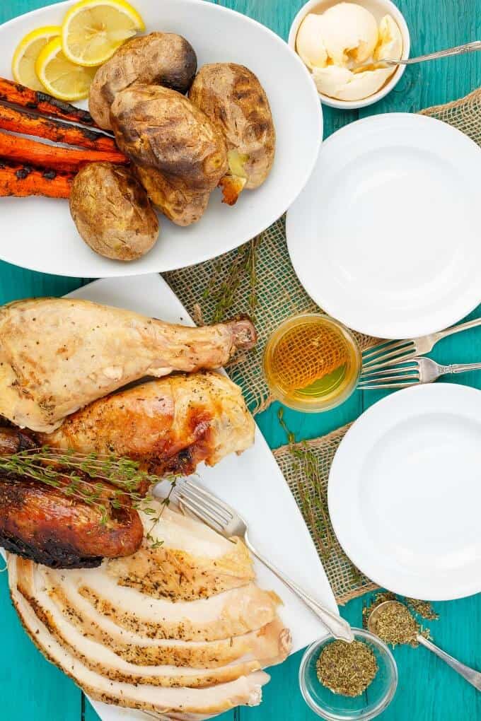 Grilled Herbes de Provence Turkey on white tray with forks and herbs. Plate with sidedish, vegetables, and ingredients on blue table