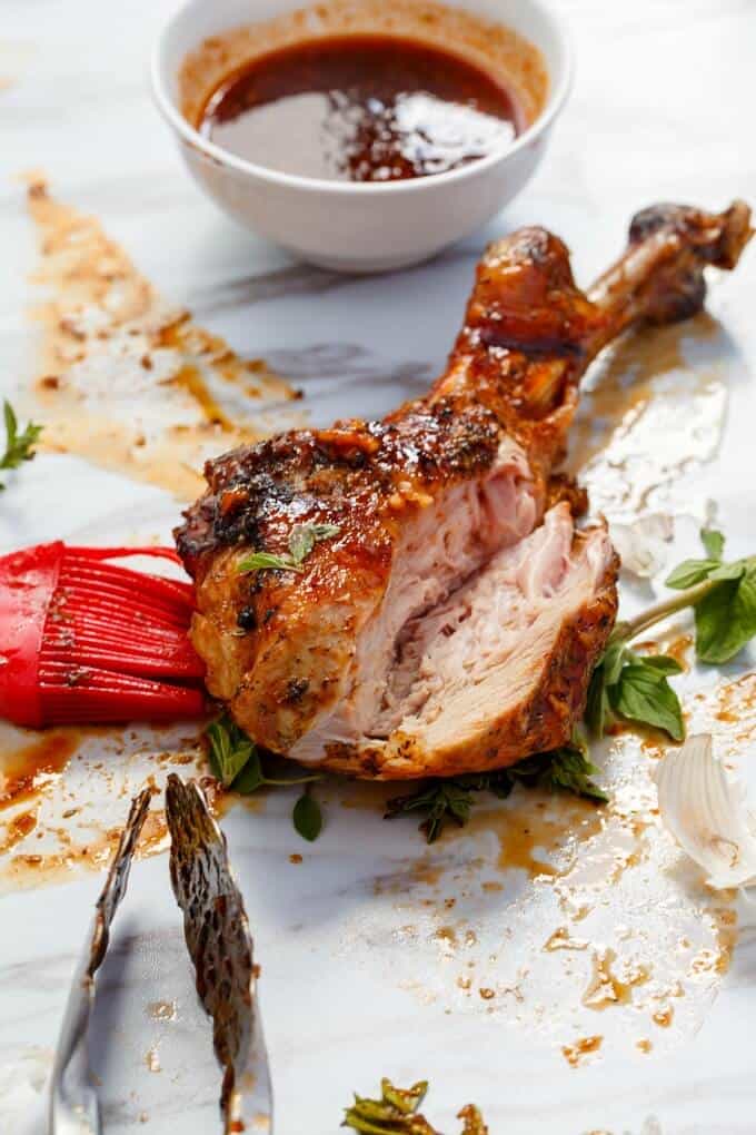 Grilled Sriracha Turkey Drumstick on white table with herbs, red brush and white bowl with sauce