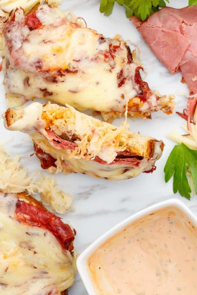 Open-Faced Reuben Sandwiches on white gray background with herbs and sauce in white bowl
