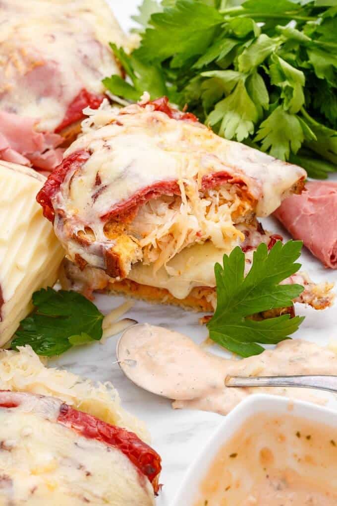 Open-Faced Reuben Sandwiches on white gray tray with herbs, sauce on spoon and in bowl