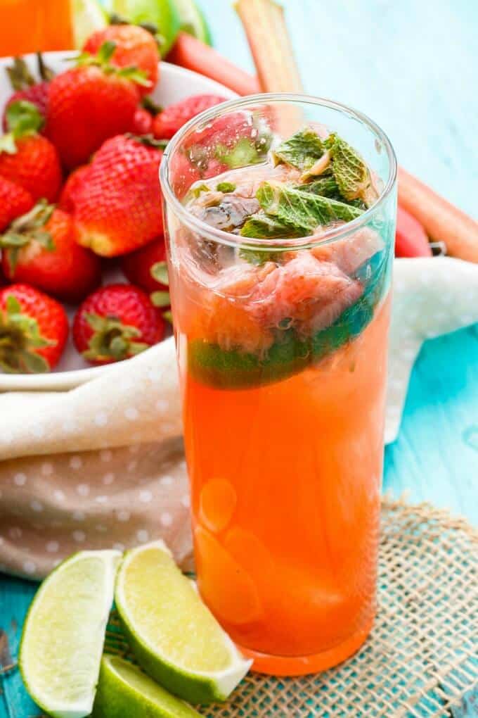 Strawberry-Rhubarb Mojito in glass cup with limes and ripe strawberries in bowl in the background