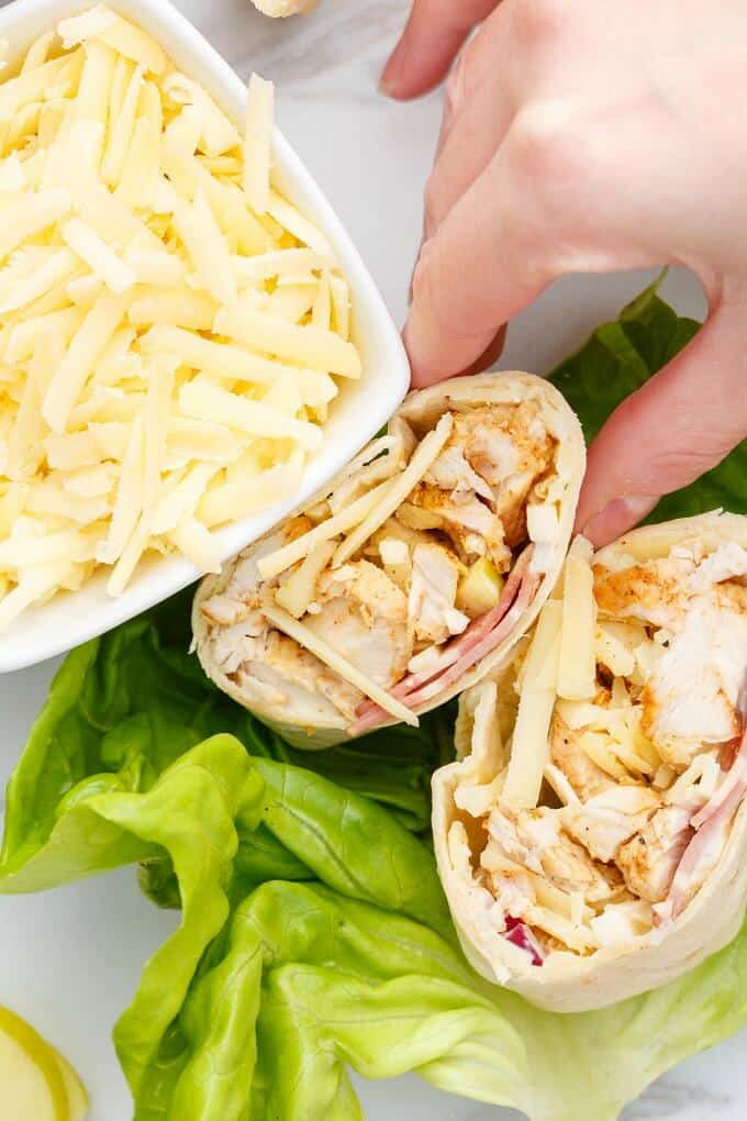 Turkey Bacon Wraps with Cheddar on lettuce touched by hand, bowl of cheddar