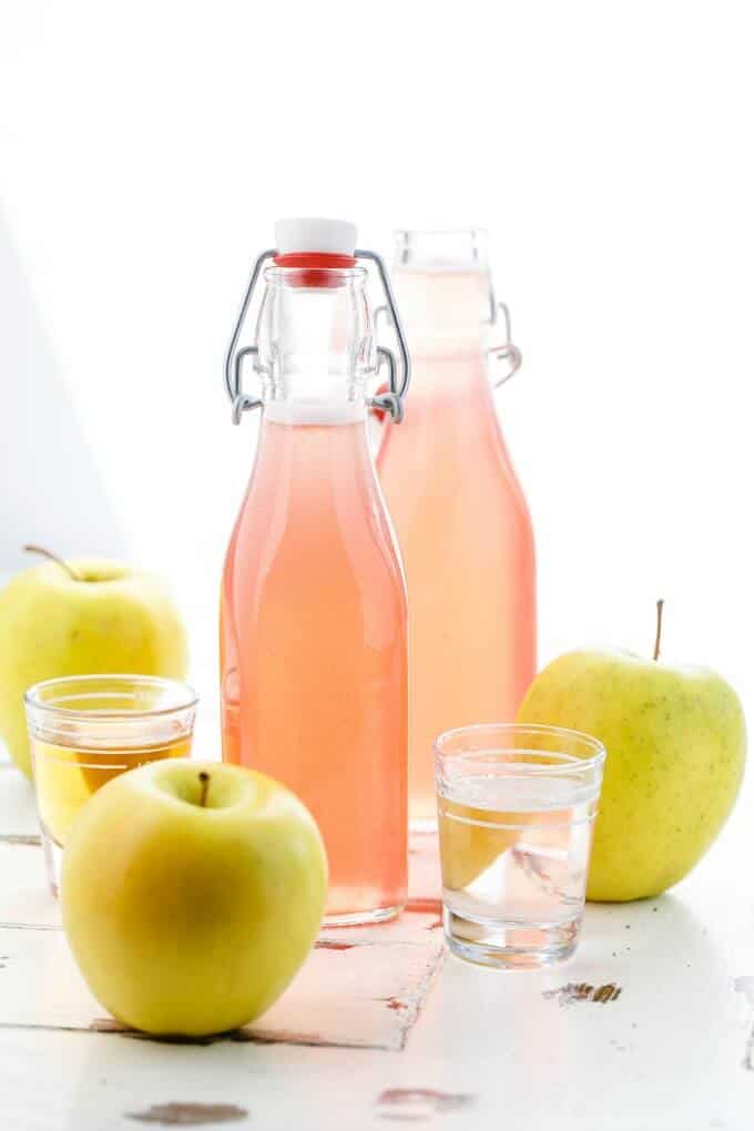 Homemade Apple-Infused Simple Syrup  in glass bottles with green apples and two glass shots