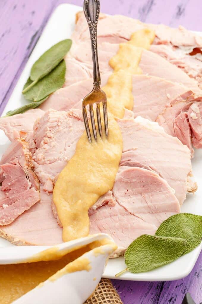 Slow Cooker Honey-Mustard Apple Ham on white tray with sauce, fork and herbs