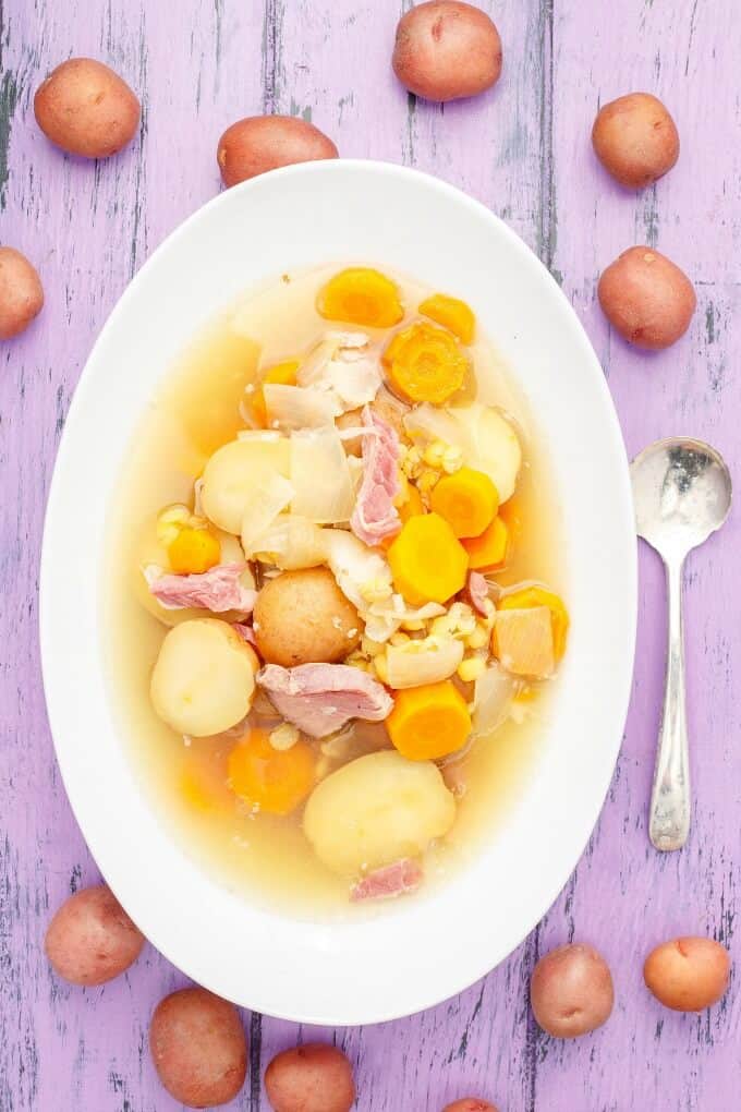 Slow Cooker Pea-Potato Soup on white plate next to spoon and scattered potatoes on purple table