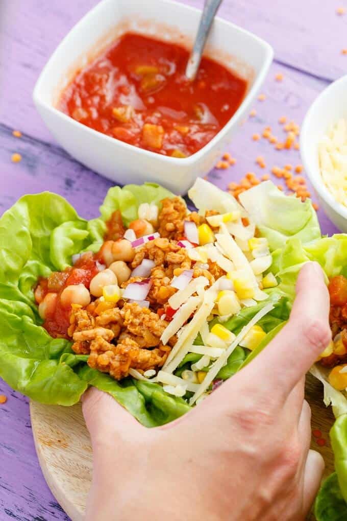 Taco Turkey-Lentil Lettuce Wraps held by hand, bowl of sauce with spoon on purple table
