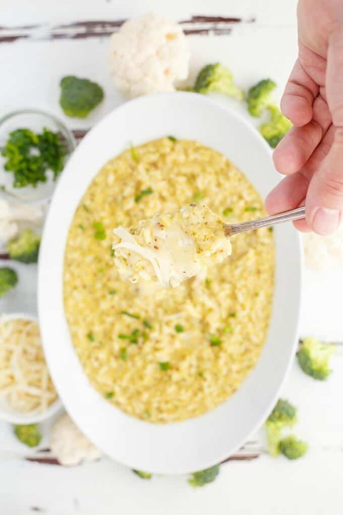 Cheesy Broccoli-Cauliflower Risotto in white bowl picked by spoon held by hand