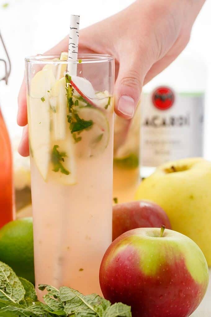 Apple Mojitos  in glass cup with straw held by hand with apples, limes around.