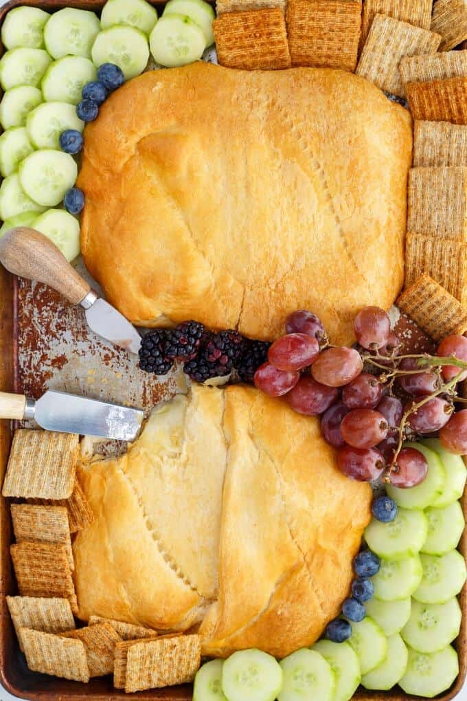 Canadian Cheese Stuffed Crescent Rolls on wooden pad with knives, crackers, grapes, cucumber, blackberries, blueberries