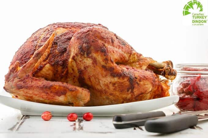 Roasted Cranberry Butter Turkey on white tray next to jar of butter, knives and scattered cranberries